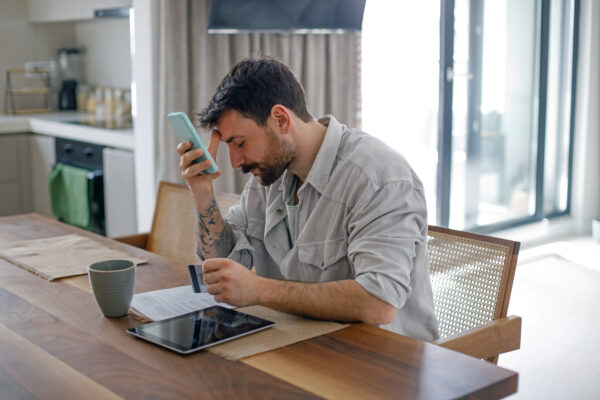 man holding a smart phone and credit card looking sad